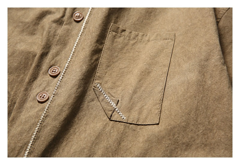 Close-up of a brown shirt’s chest pocket and front placket with buttons and pale decorative stitching.