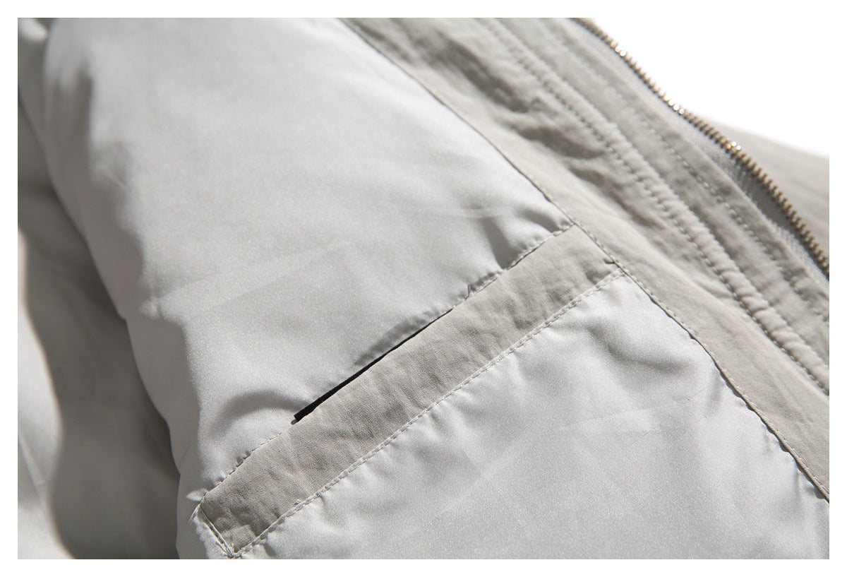 Close-up of a gray jacket's angled welt pocket and stitching beside the zipper.