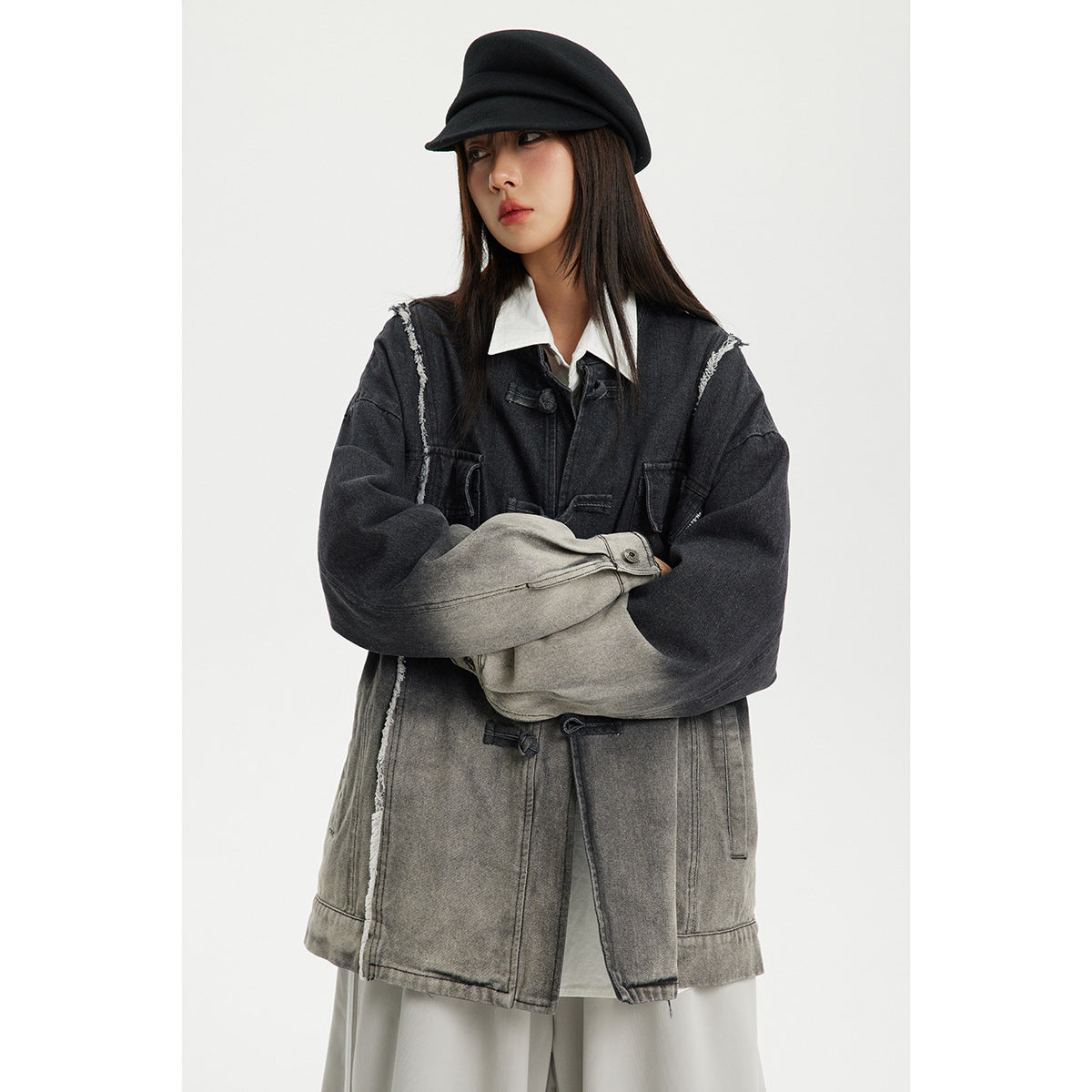 Model wearing an oversized charcoal-to-gray ombré jacket with frayed seams and toggle closures, layered over a white shirt.