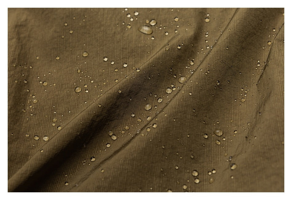 Close-up of olive-brown fabric with water droplets beading across its folded surface.