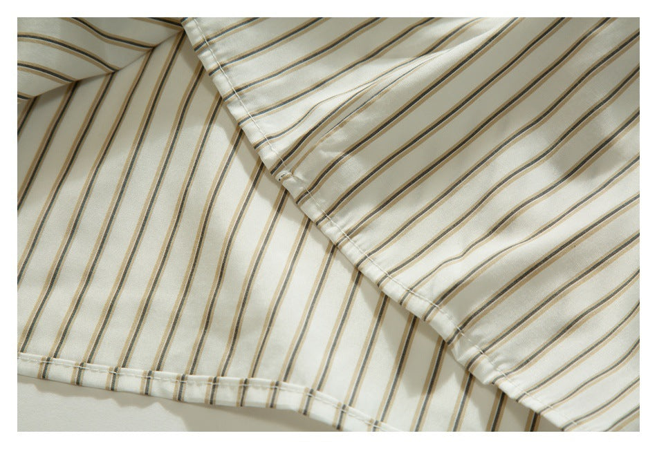Close-up of overlapping ivory shirt fabric with tan and dark gray stripes, stitching, and a small button.