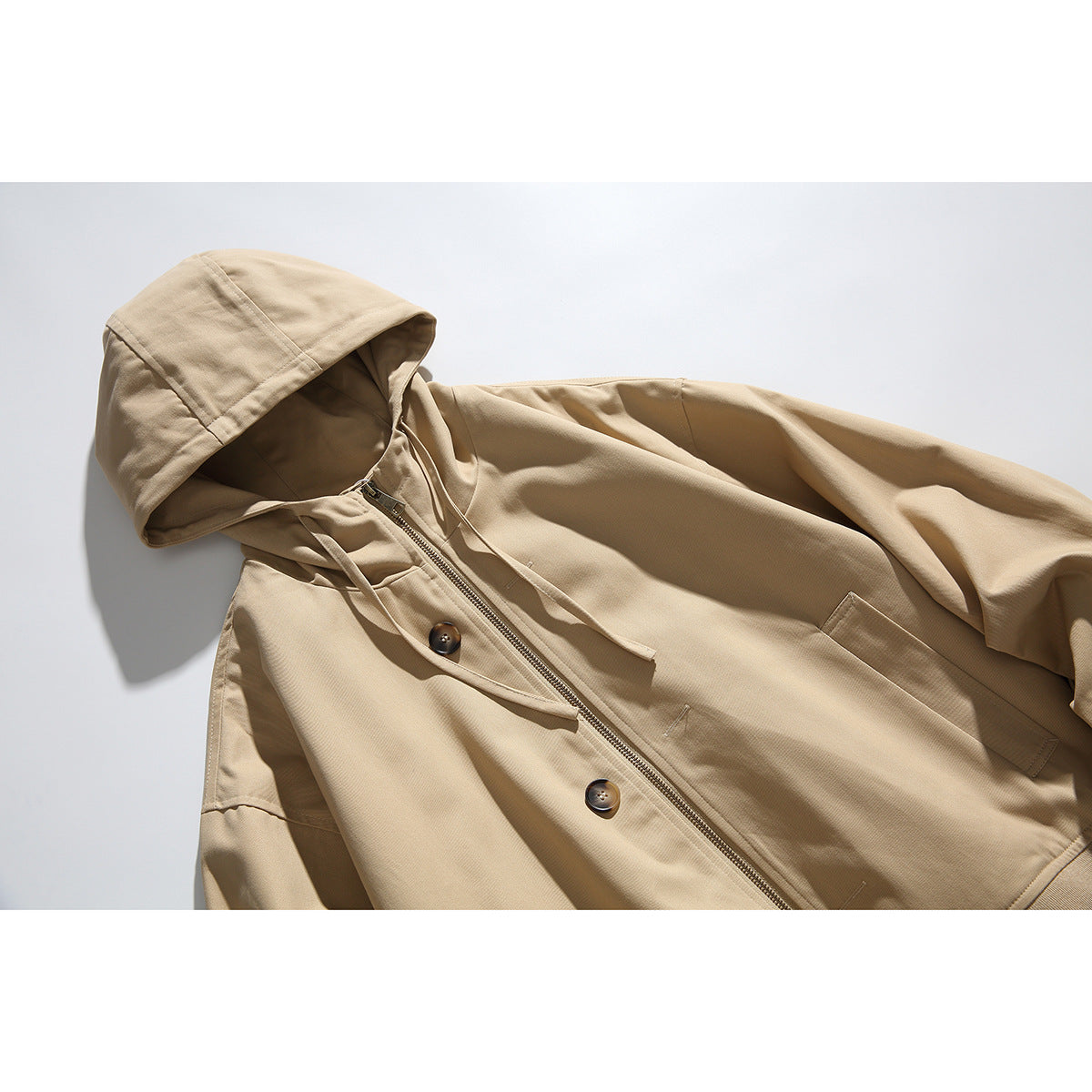 Close-up of a beige hooded jacket laid flat, showing the drawstrings, zipper, buttons, and front pockets.