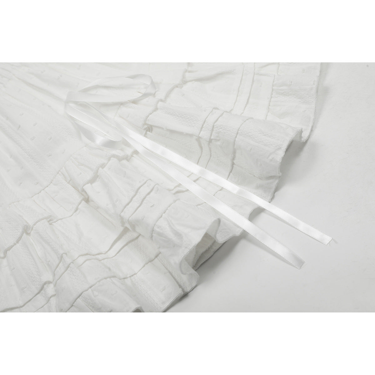 Close-up of a white tiered skirt with textured panels and long satin waist ties.