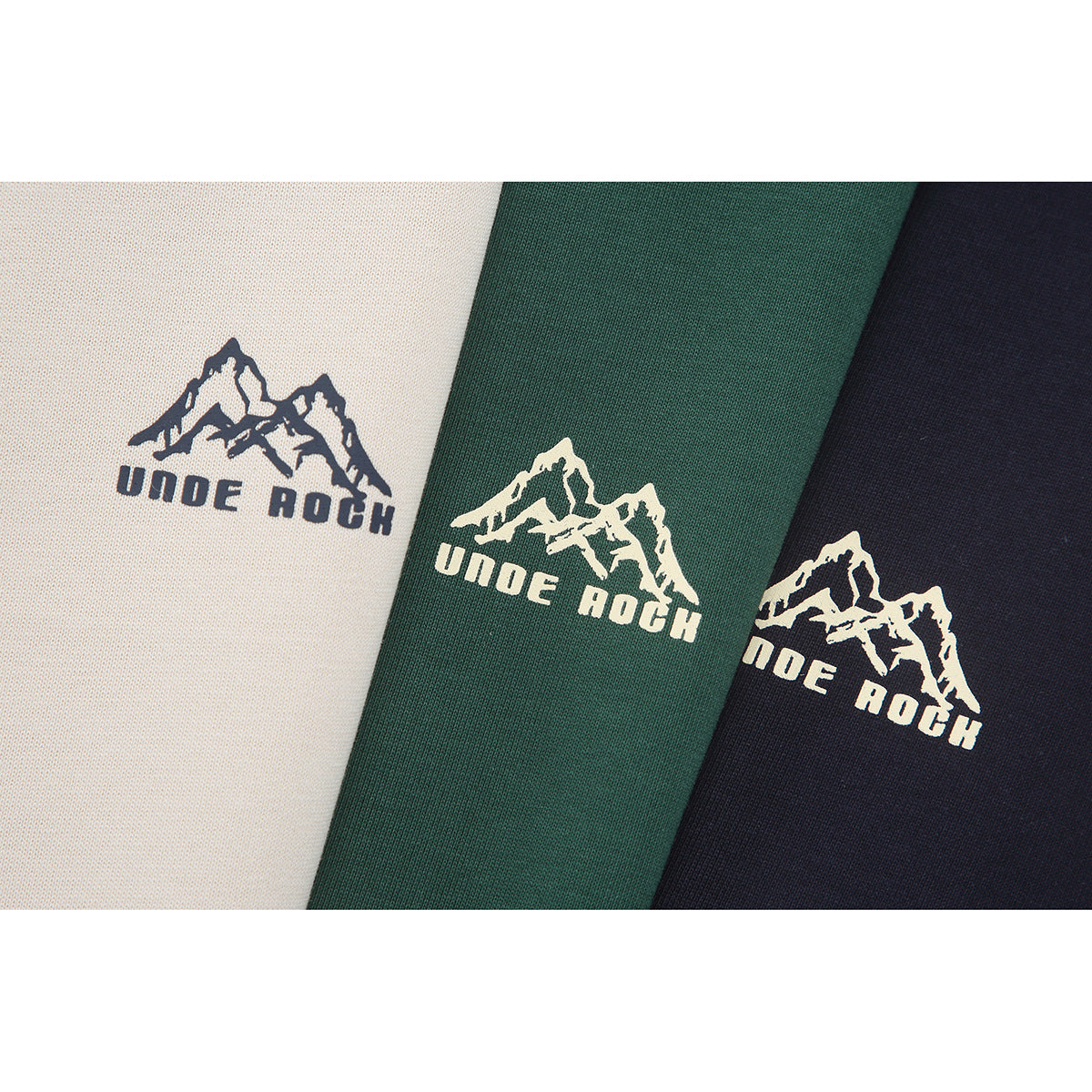 Close-up of the mountain logo on cream, forest-green, and navy T-shirt fabric.