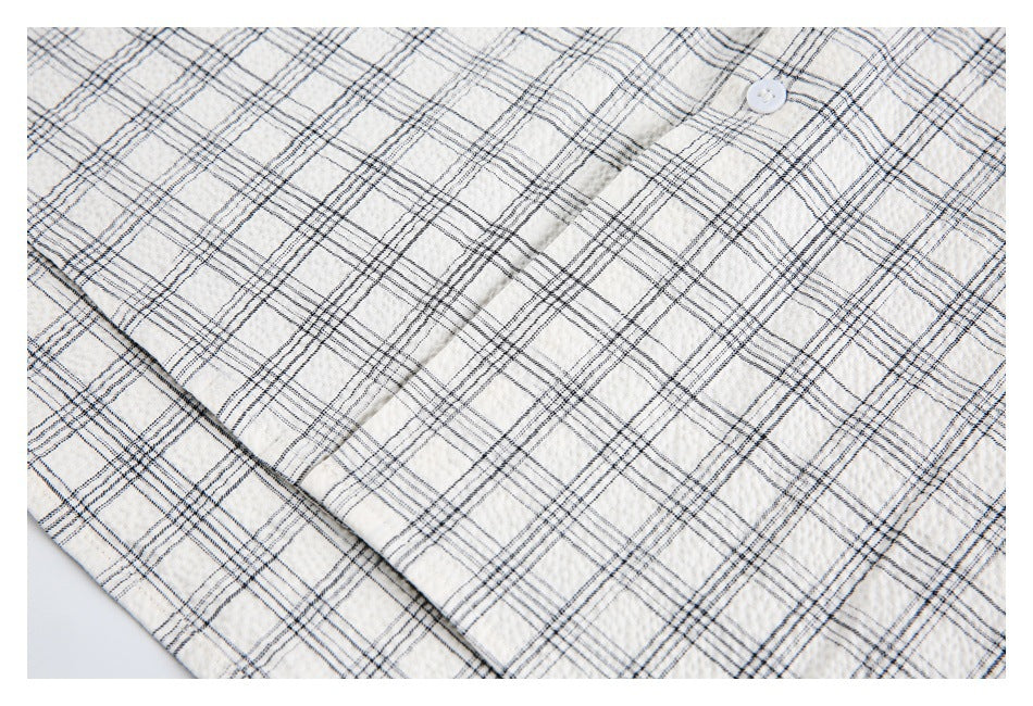 Close-up of an off-white plaid garment showing a white button and overlapping fabric panels.