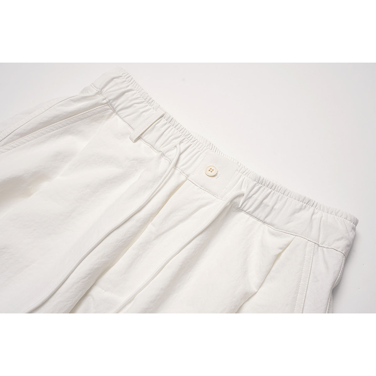 Close-up of white pants showing the gathered waistband, button, belt loops, and front pleats.