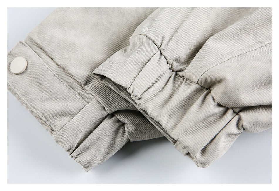 Close-up of a gathered elastic cuff and snap-button tab on a light gray jacket.