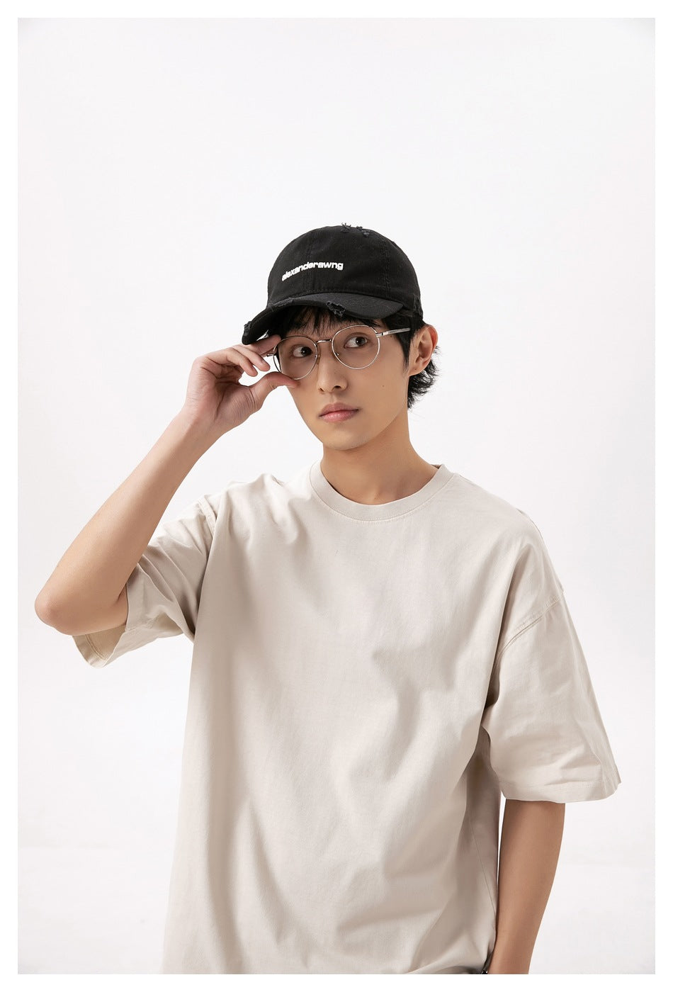 Close view of a model wearing a loose cream short-sleeve T-shirt and a black cap.