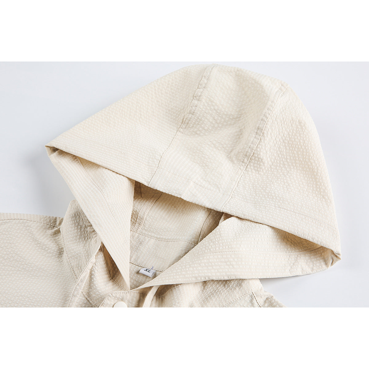 Close-up of a cream textured garment’s hood, with an XL size tag visible inside.