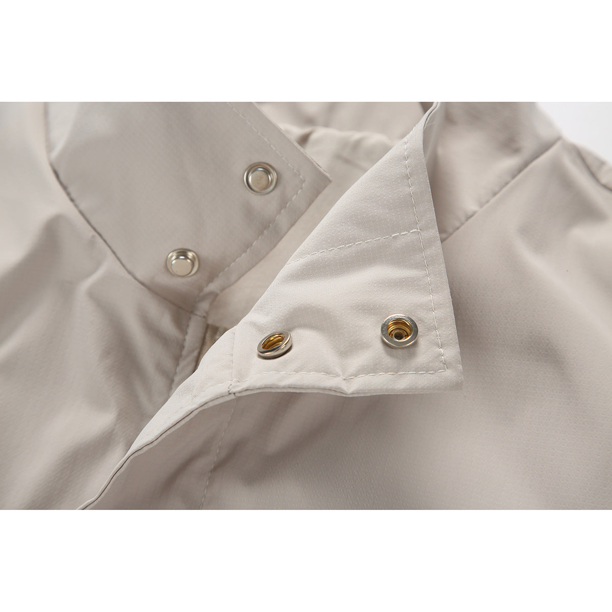 Close-up of the light beige jacket's open front placket with metal snap fasteners.