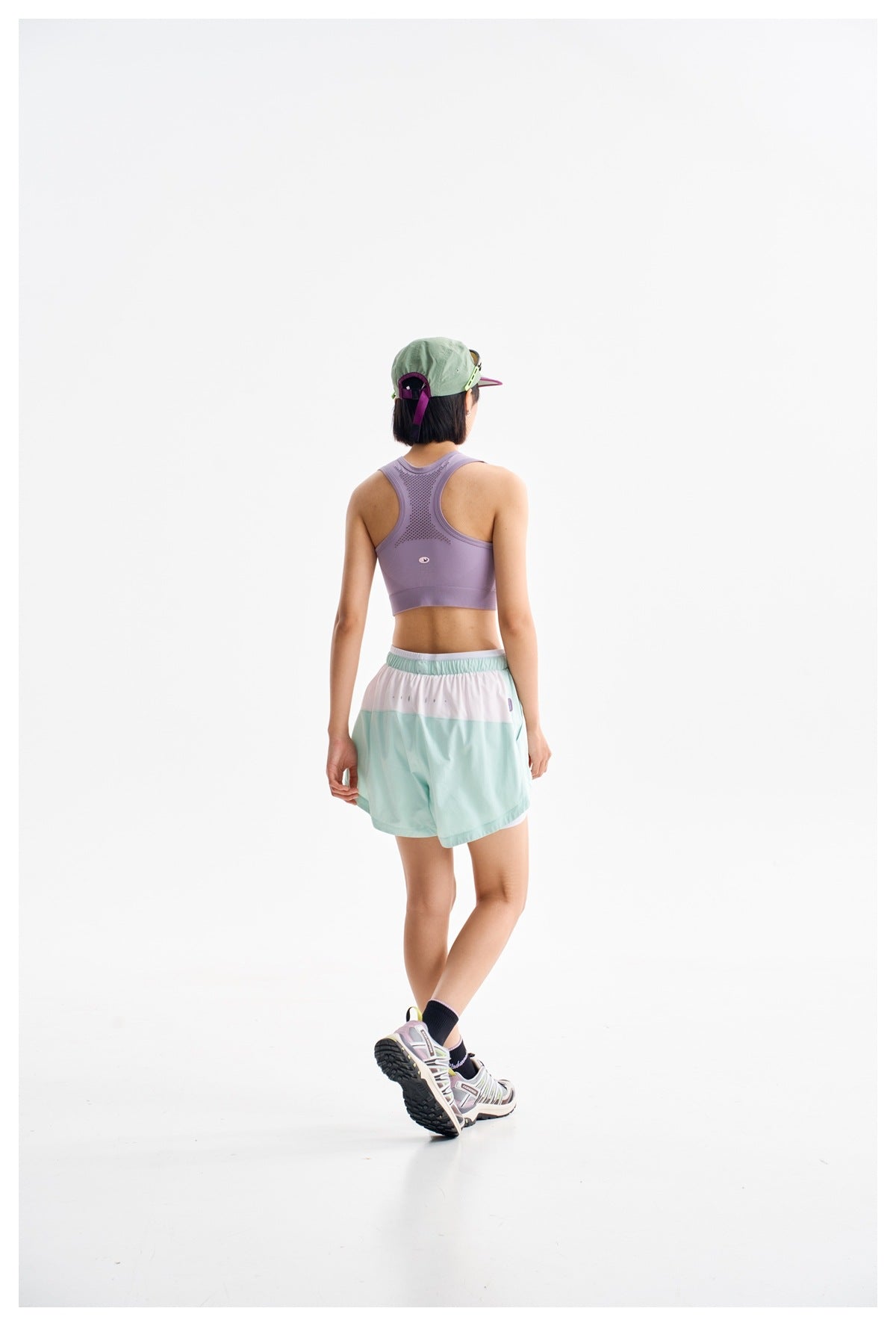 Back view of a model wearing a lavender racerback sports bra and mint shorts with a white waistband panel.