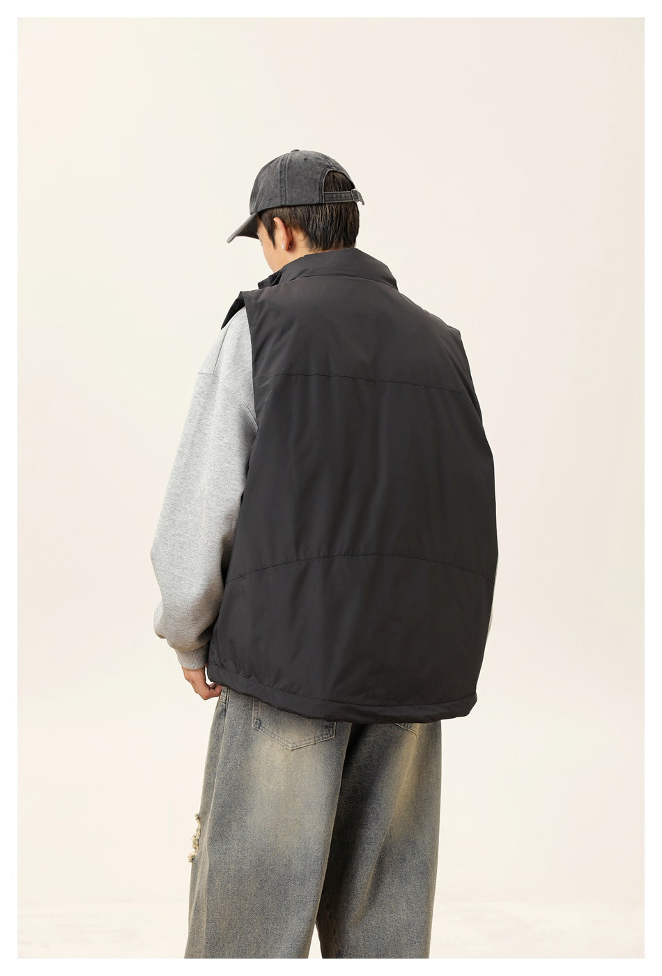 Rear three-quarter view of a model wearing a black sleeveless vest over a gray sweatshirt.