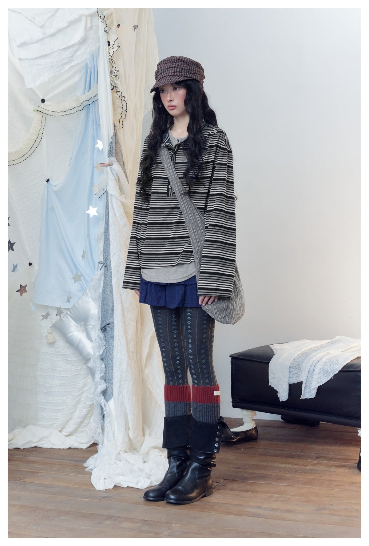 Full-length view of a model in a black and gray striped henley, navy skirt, patterned tights and black boots.
