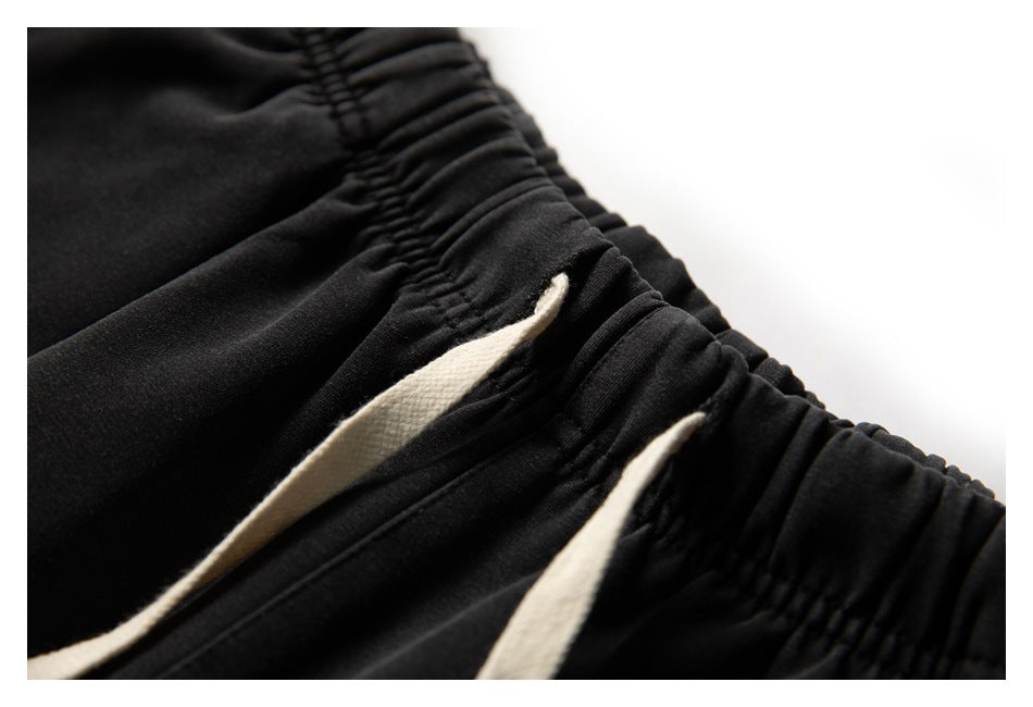 Close-up of black jogger pants with a gathered elastic waistband and cream drawstrings.