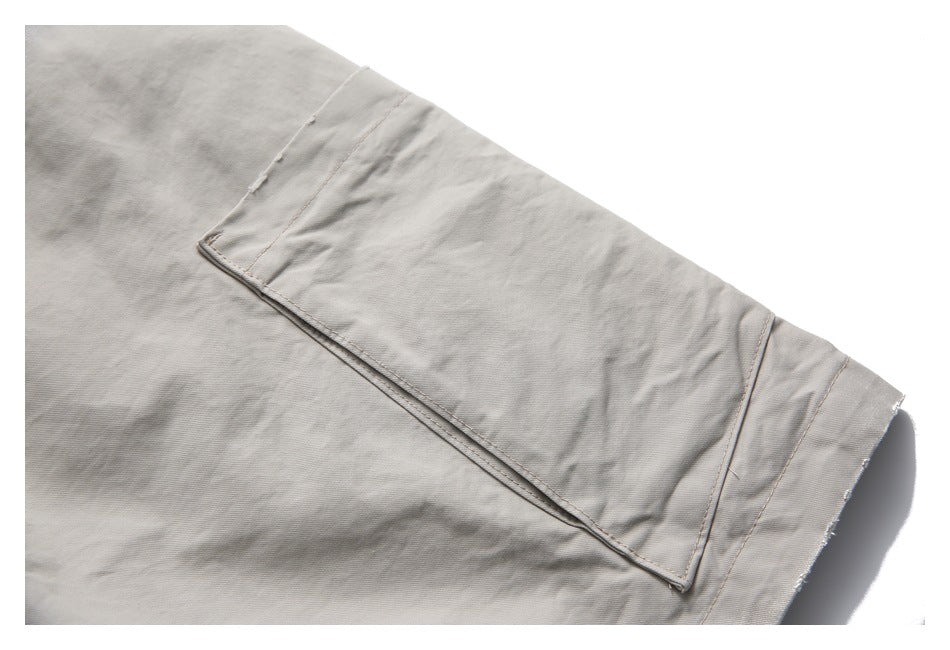 Close-up of a large rectangular pocket and hem on light gray-beige shorts.