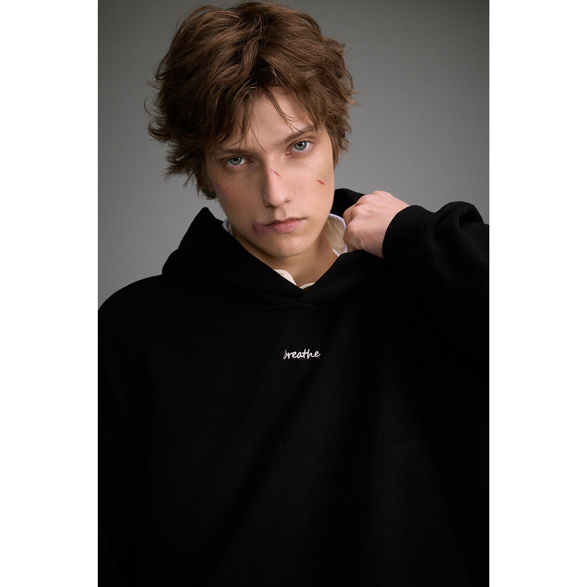 Close portrait of a model in a black hoodie with small white “breathe” script on the chest.