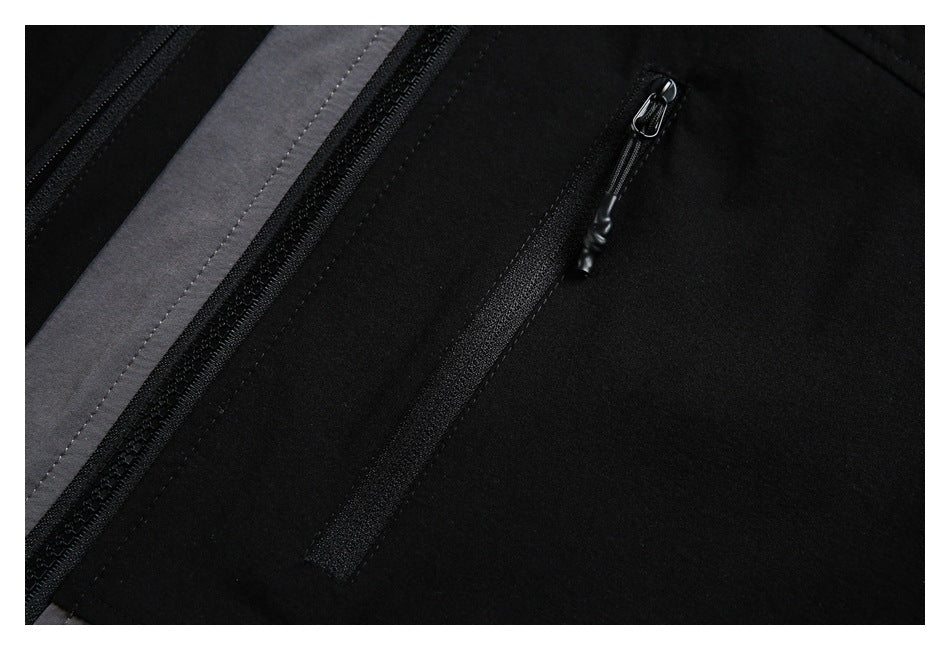 Close-up of a black garment with a charcoal-gray panel and a vertical zip pocket.