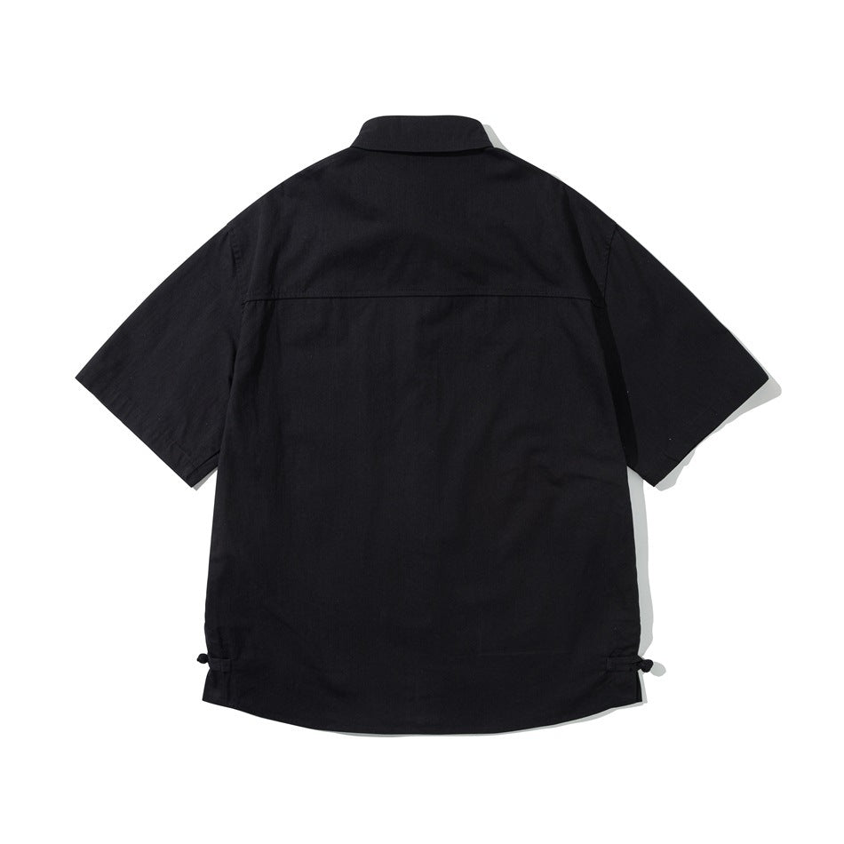 Black short-sleeve shirt, back view flat lay, with back yoke seam and knot-button loops at side hems