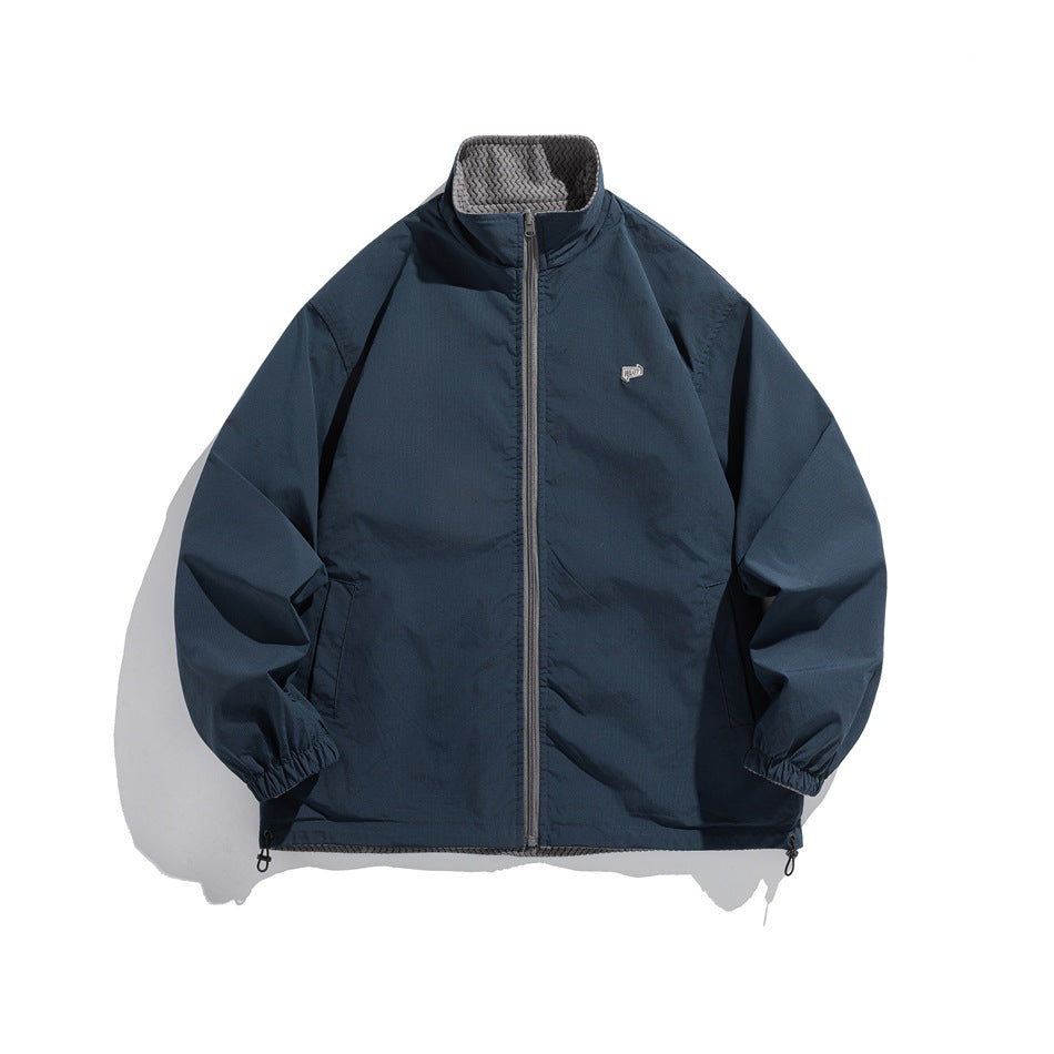 Front view of a navy zip jacket with a raised collar, patterned lining, side pockets and gathered cuffs.