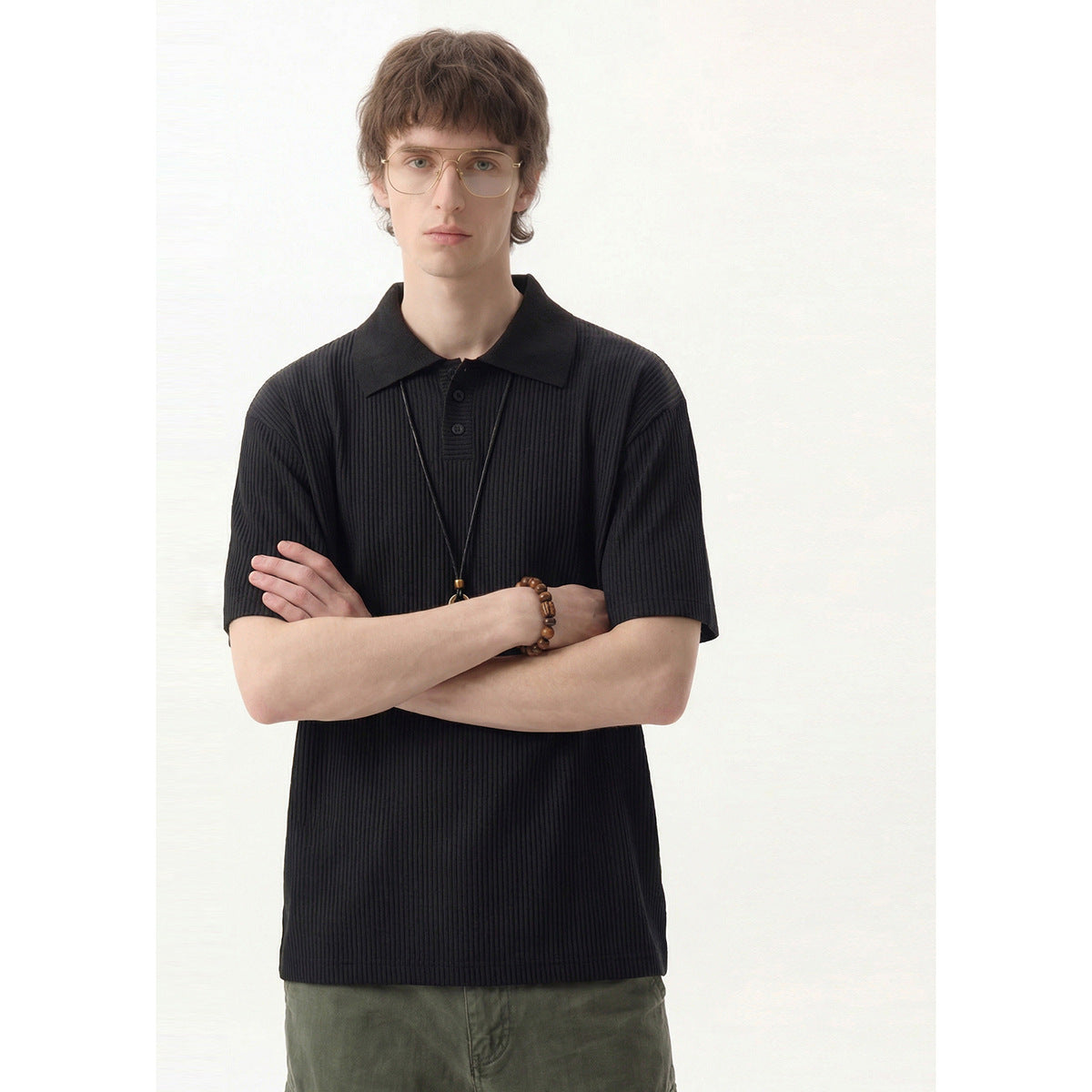 Model wearing a black vertically ribbed short-sleeve polo shirt with a pointed collar and button placket.