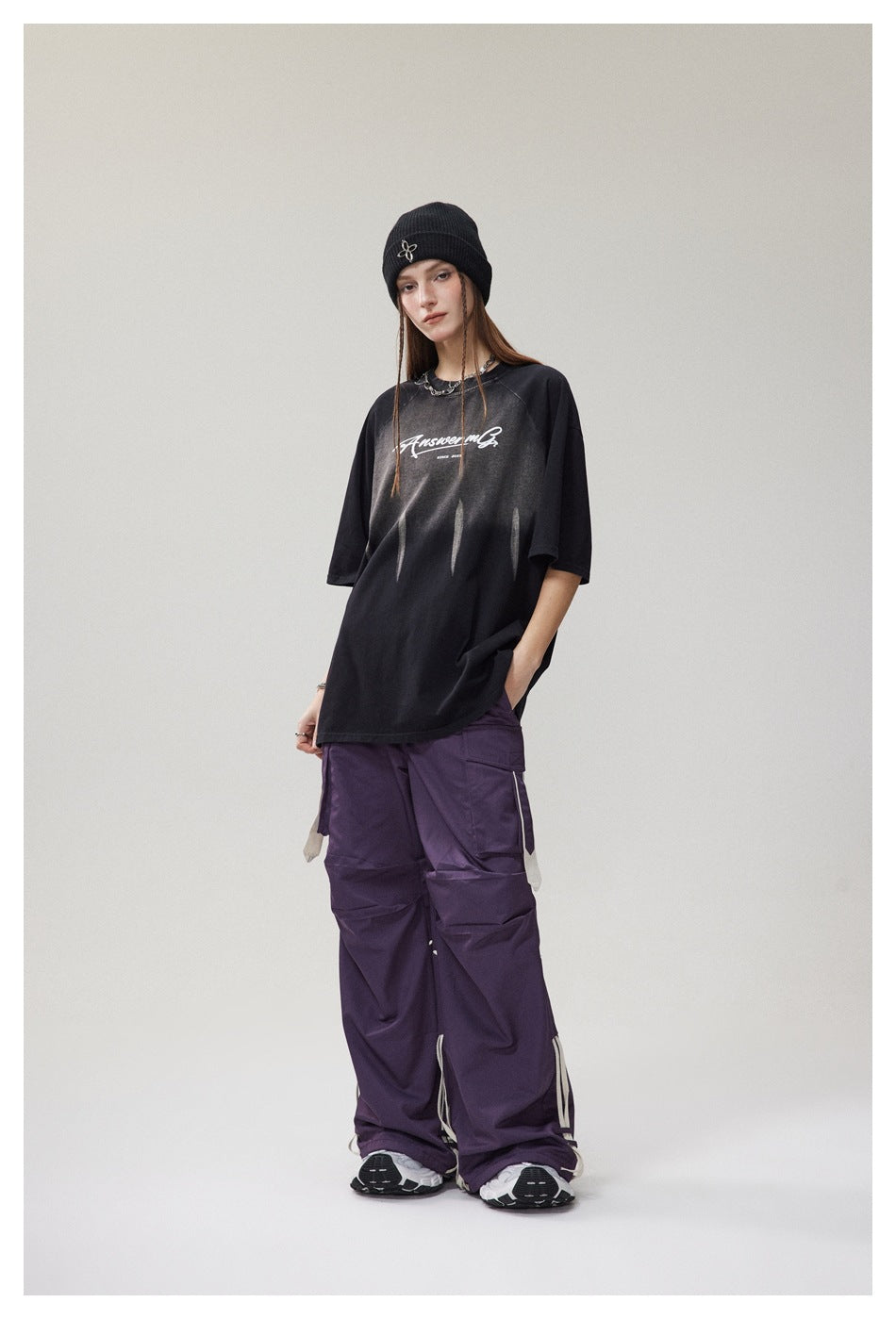 Model wearing an oversized black T-shirt with white chest lettering and pale streak graphics, paired with purple cargo pants.