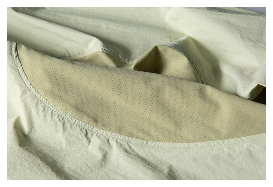 Close-up of pale sage garment fabric and a curved section of beige perforated mesh lining.