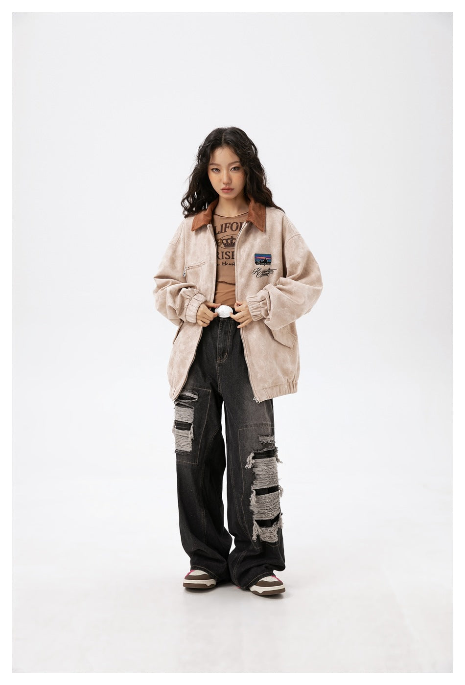 Model wearing an open beige-khaki oversized jacket with brown collar over a brown tee and ripped black jeans, front view
