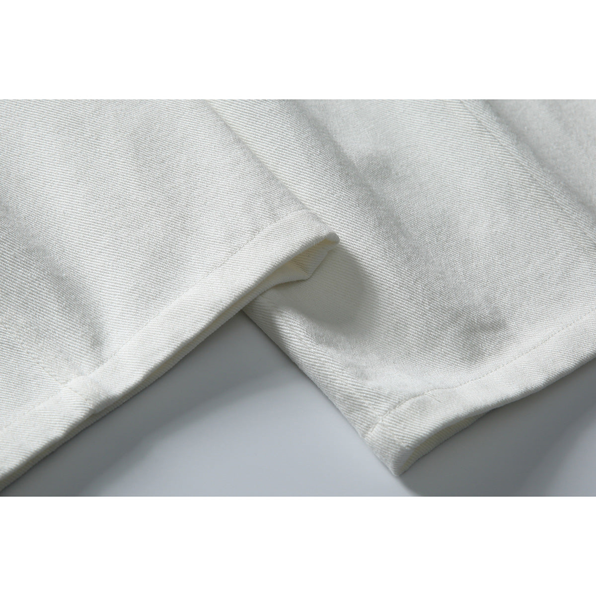 Close-up of the stitched hems and legs of white trousers.