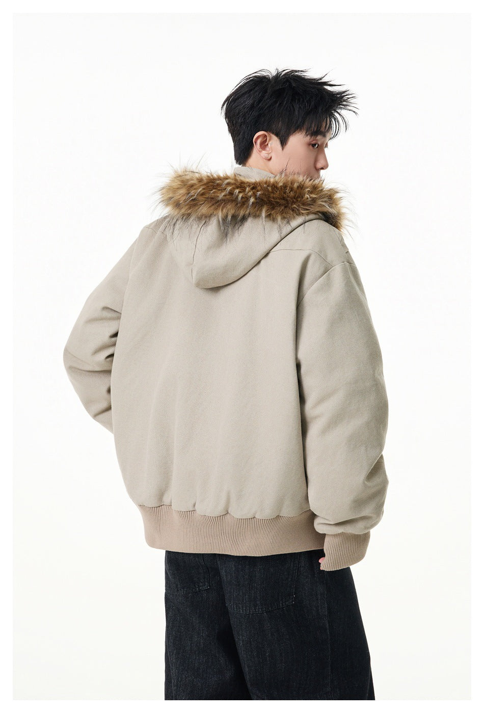 Rear view of a model wearing a light beige hooded jacket with tan fur trim and a ribbed hem.