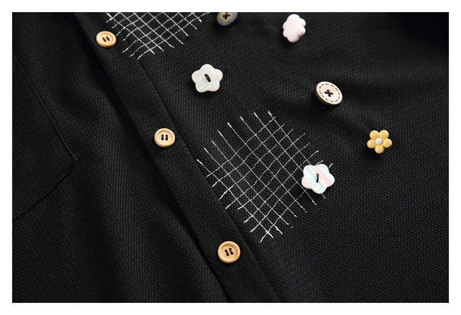 Close-up of a black garment with tan buttons, white crosshatch stitching, and decorative flower-shaped buttons.