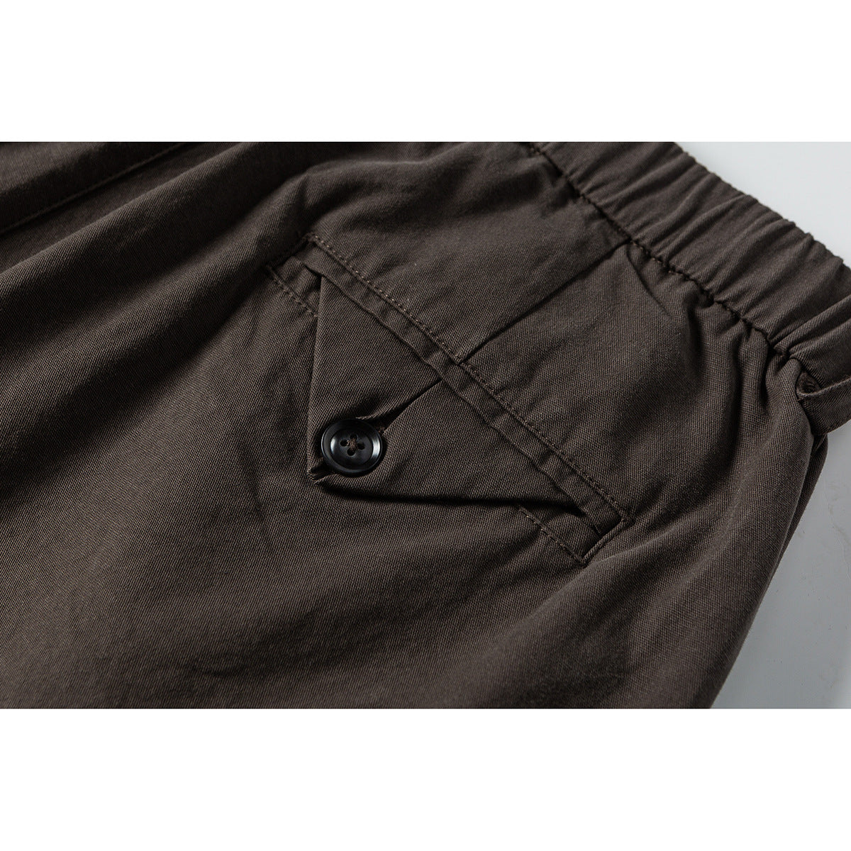 Close-up of brown trousers showing an elastic waistband and a buttoned flap pocket.