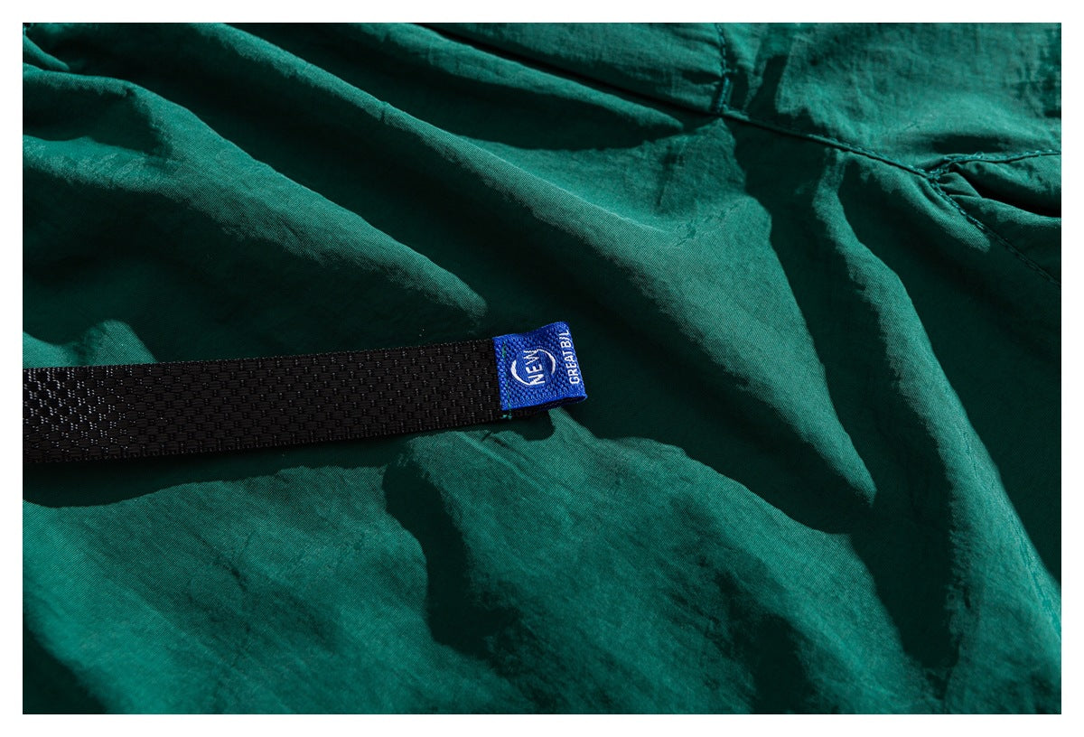 Close-up of teal shorts with a black webbing strap and a small blue fabric tag.