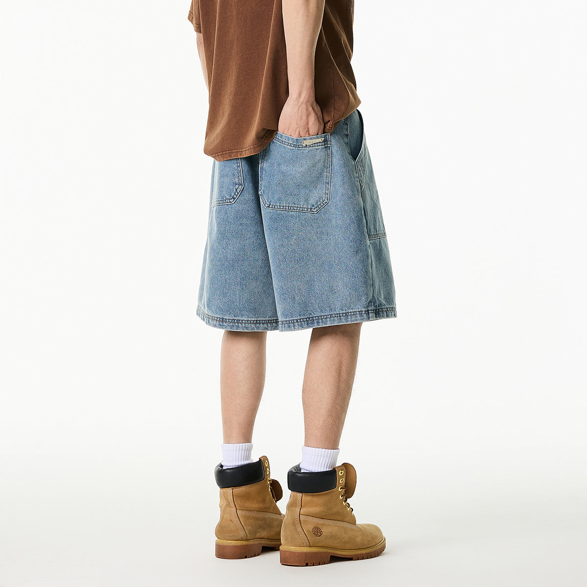 Rear three-quarter view of a person wearing loose light-wash denim shorts with back pockets.