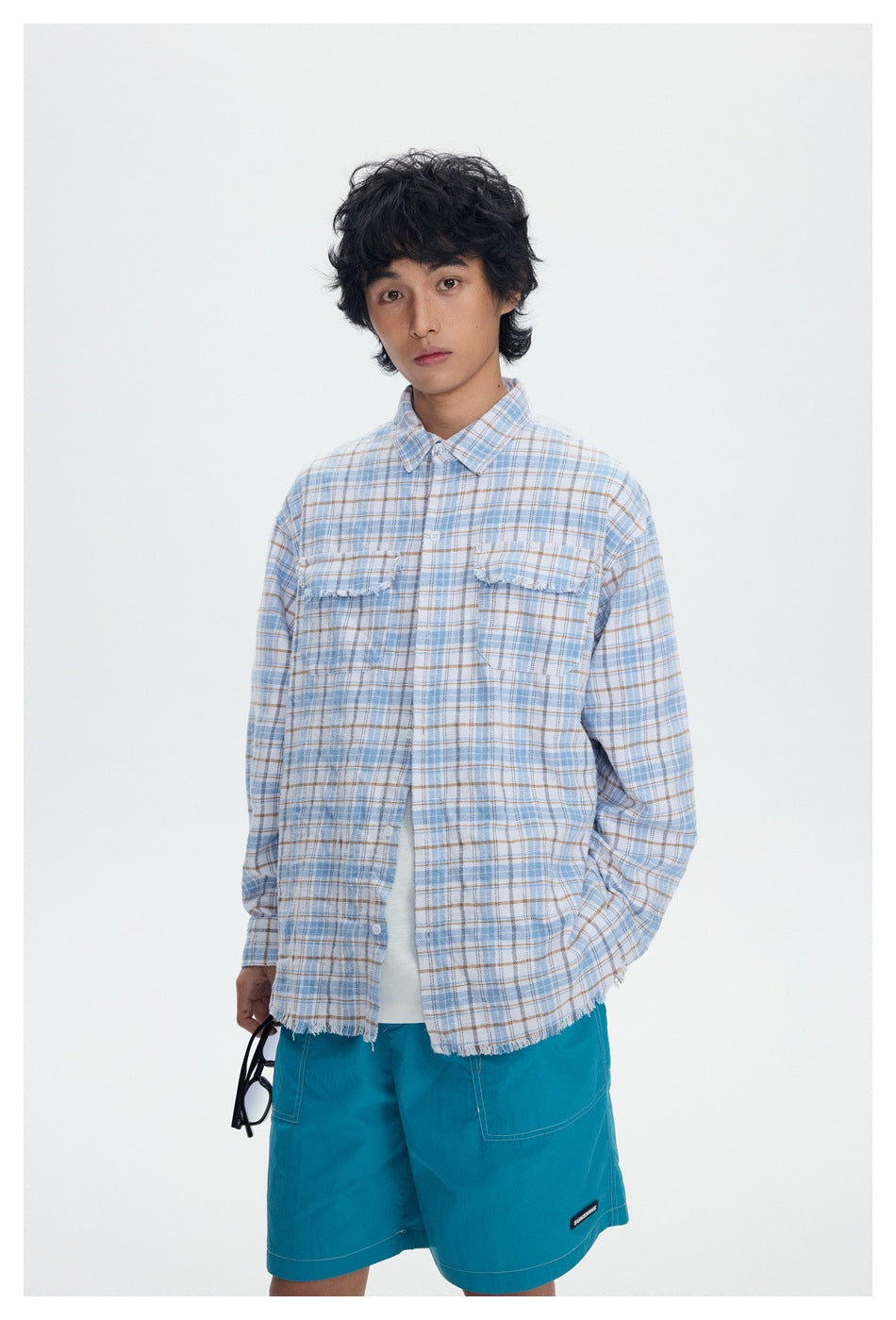 Model wearing a pale blue and tan plaid button-up shirt with two chest pockets and teal shorts.