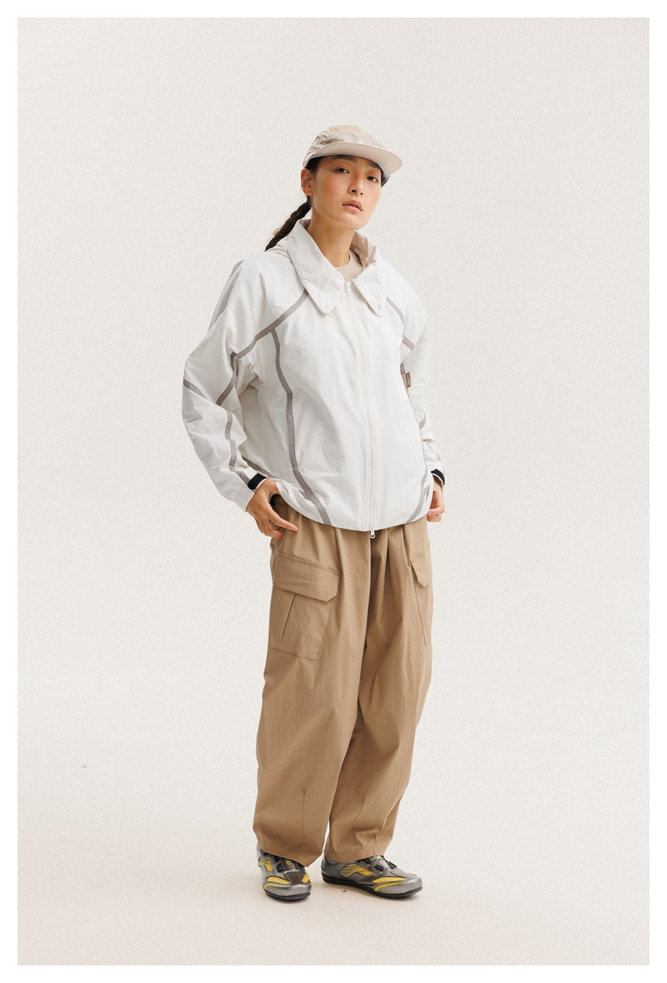 Model wearing a white zip-front jacket with gray piping and tan cargo pants, shown from the front.