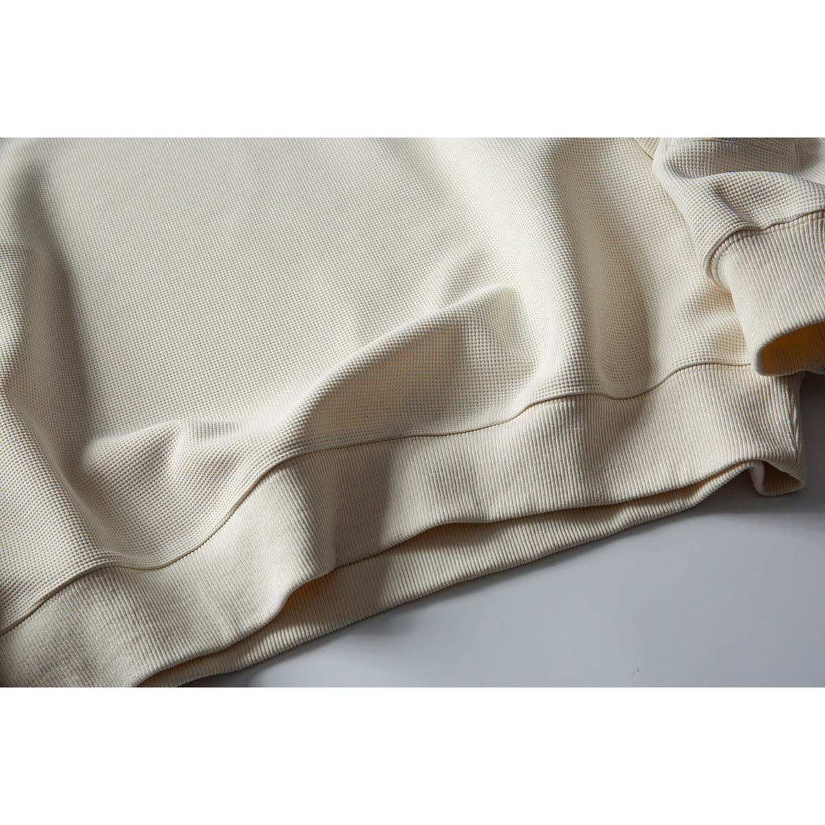 Close-up of the ivory waffle-knit sweatshirt’s textured body and wide ribbed hem.