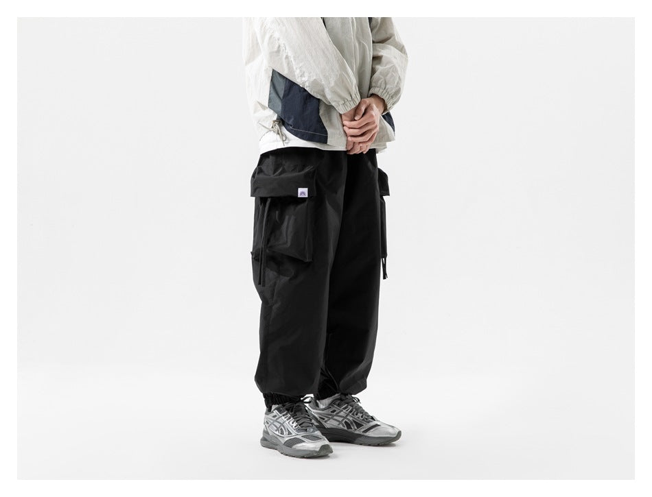Rear-side view of a model wearing black cargo jogger pants with large flap pockets and elastic cuffs.