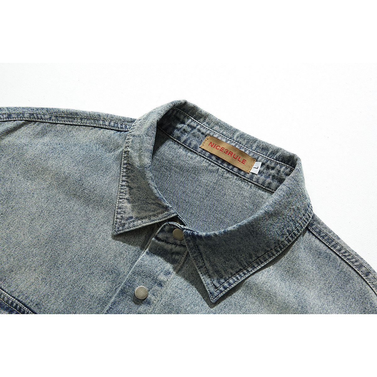 Close-up of a faded blue denim shirt collar, stitching, metal snap, and sewn neck label.