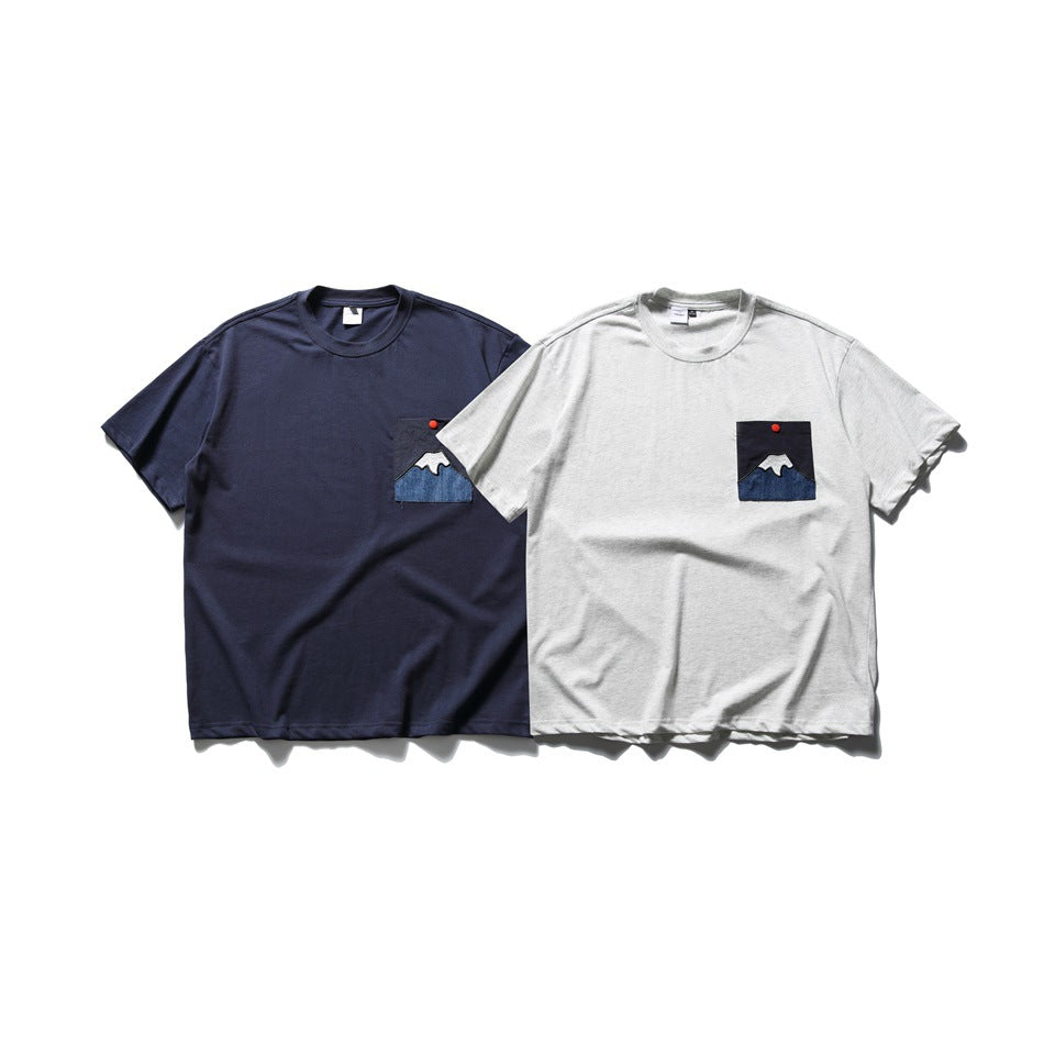 Two short-sleeve T-shirts, one navy and one light gray, each with a chest pocket and mountain appliqué.