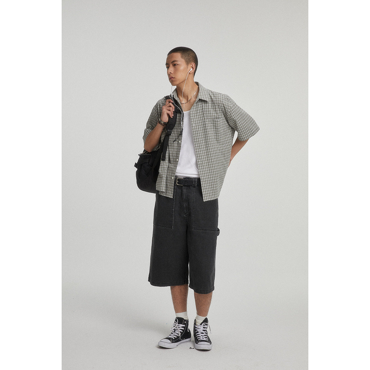Model wearing a gray checked short-sleeve shirt over a white tank and black knee-length shorts.