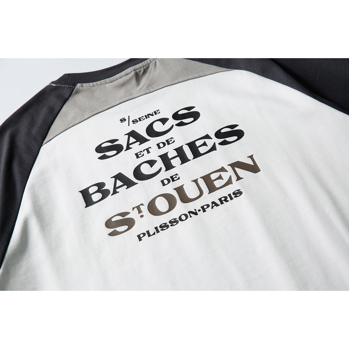 Close-up of the back of a white, gray, and charcoal color-block T-shirt with large printed lettering.