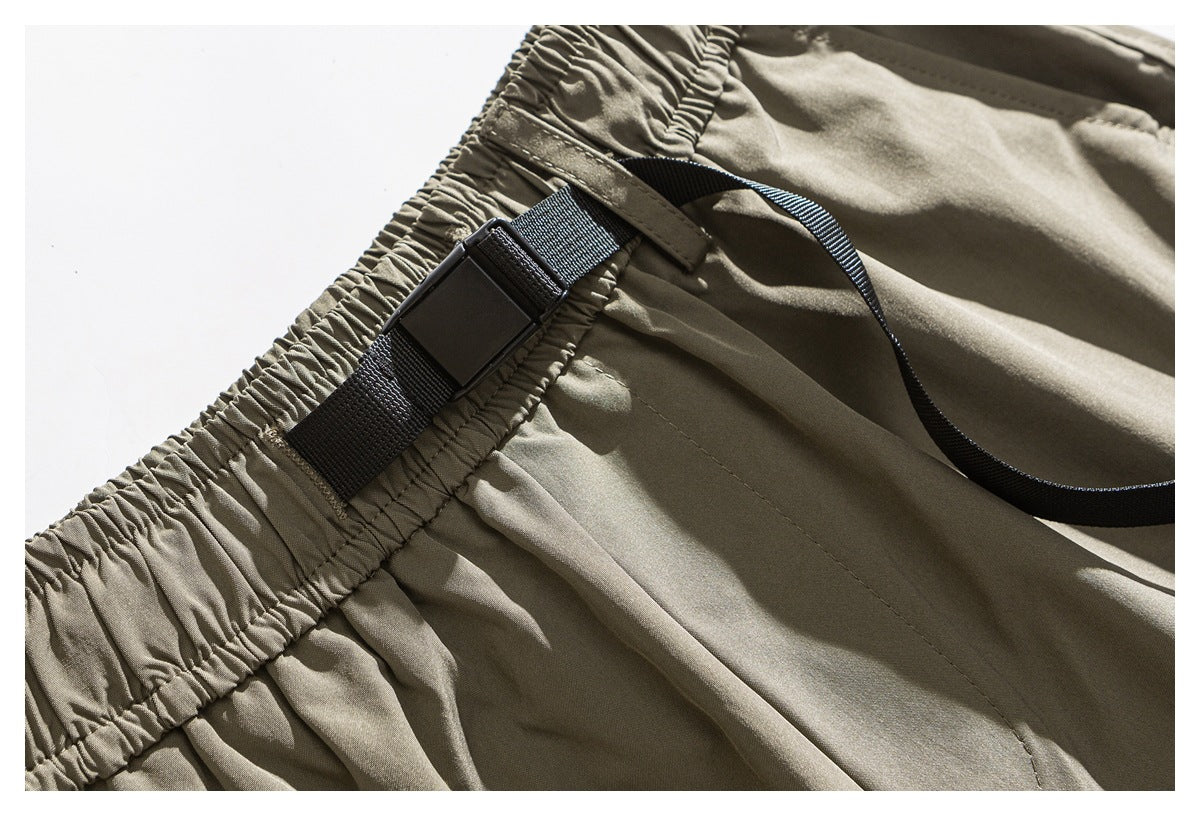 Close-up of khaki trousers showing a gathered elastic waistband and black webbing strap with buckle.