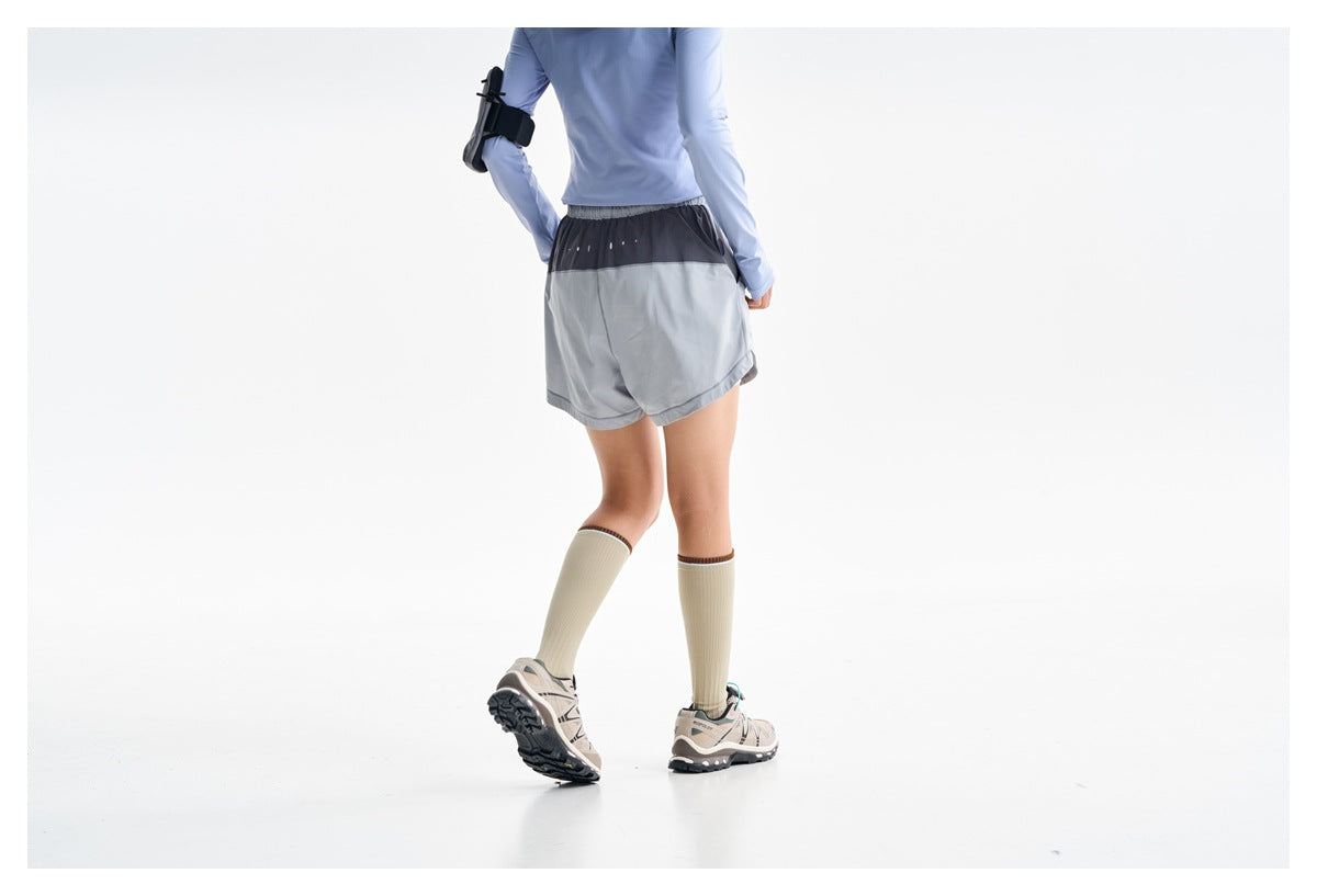 Rear view of a model wearing gray running shorts with a dark upper panel, styled with a light blue top and knee-high socks.