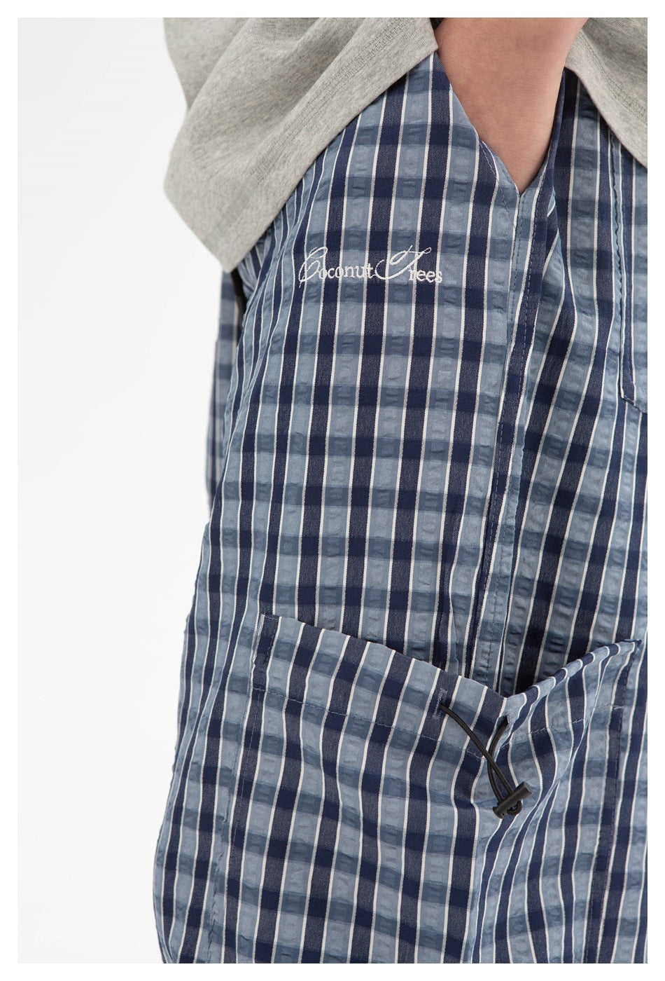Close view of a person wearing blue and gray plaid pants with white embroidered lettering and a black drawcord toggle.