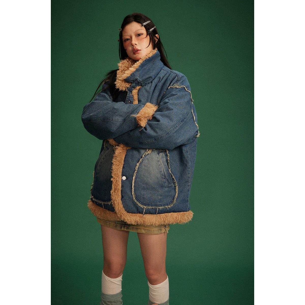 Model wearing an oversized blue denim jacket with tan shaggy trim and large patch pockets, arms crossed.