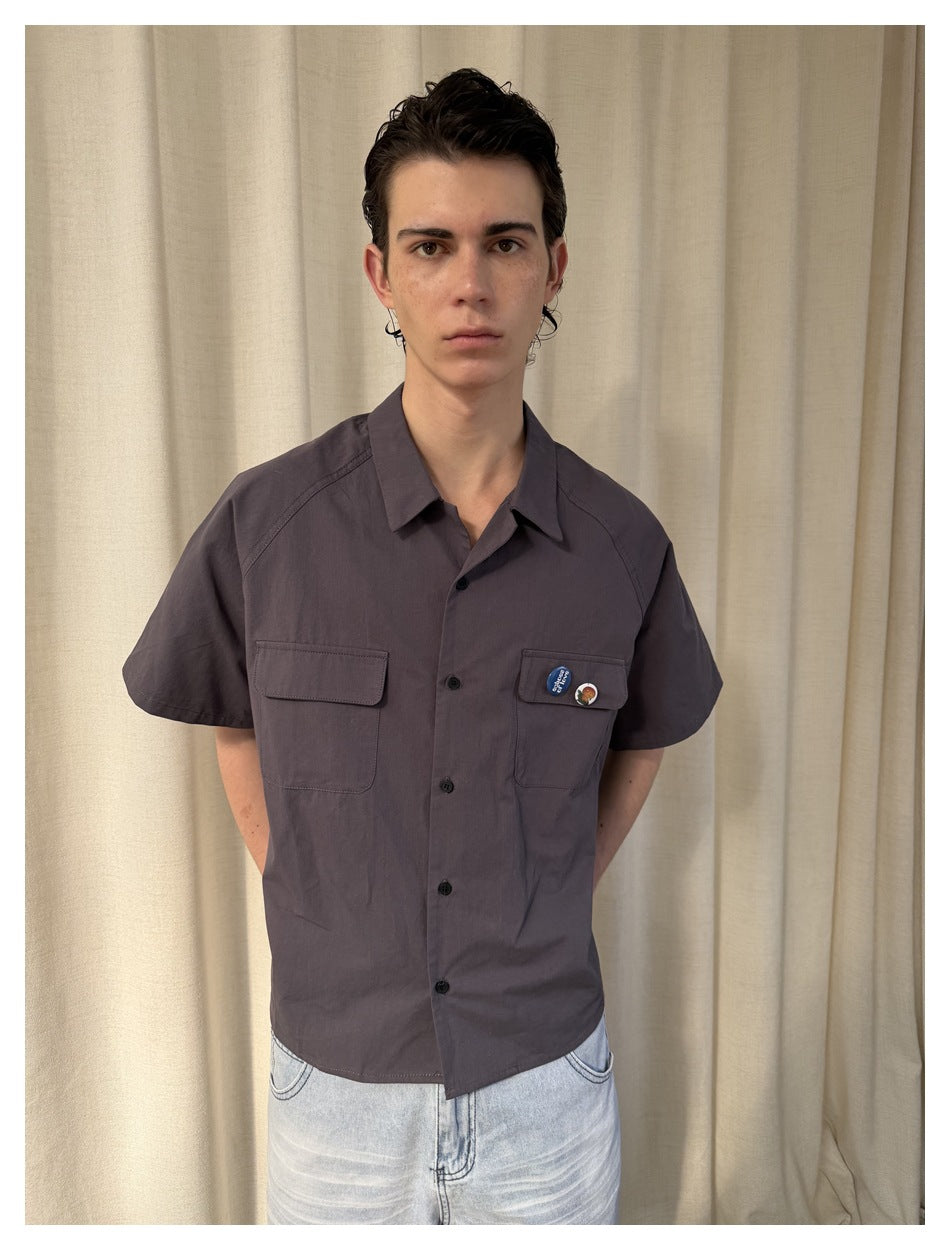 Closer front view of a model in a charcoal short-sleeve button-up shirt with two flap pockets and small pins.