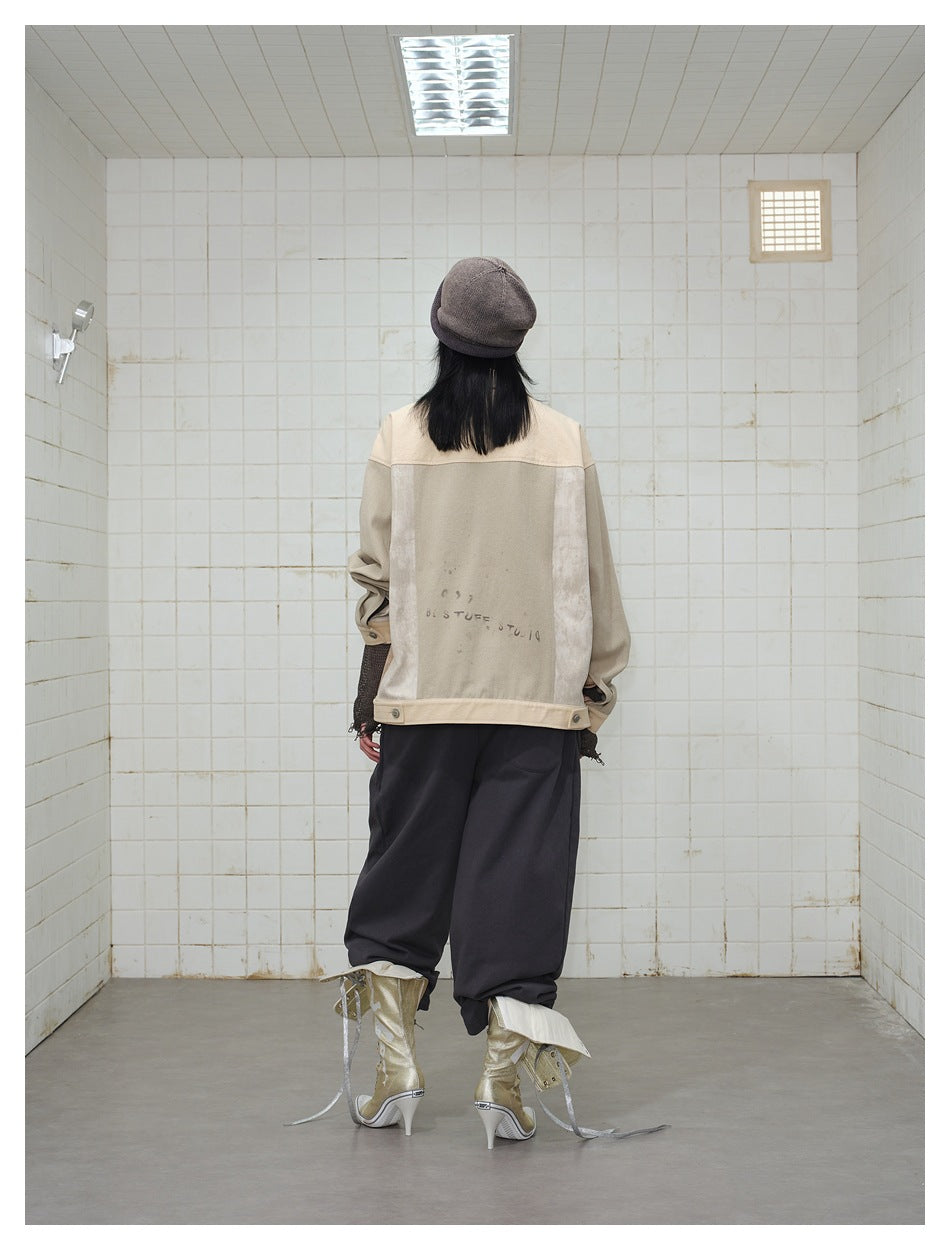 Back view of a model wearing a beige patchwork jacket with a large pale back panel and dark trousers.
