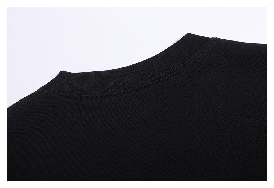 Close-up of a black garment’s crew neckline and stitching against a light background.