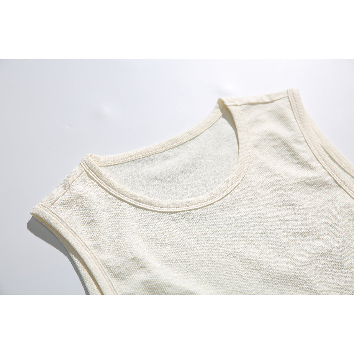 Close-up of the cream tank top's rounded neckline and bound armhole edge.