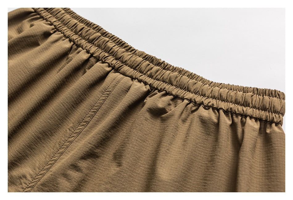 Close-up of the gathered elastic waistband and pocket stitching on tan shorts.
